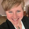 A JCU faculty member with short blonde hair and blue eyes smiles warmly, presenting herself in a black blazer and silver