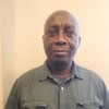 A JCU faculty member, a bald man with dark skin, smiles gently for his portrait, wearing a dark green shirt.