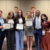 Nine students pose together, holding certificates; they smile for the camera, celebrating an event.