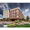 A modern multi-story brick and stone building stands behind colorful landscaped gardens under a dramatic cloudy sky.