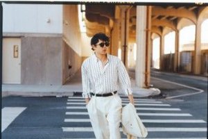 A man wearing sunglasses and light-colored striped shirt walks confidently across a crosswalk under an overpass.