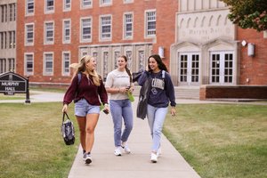 Three Young Women Walk Talk Sidewalk Front Brick